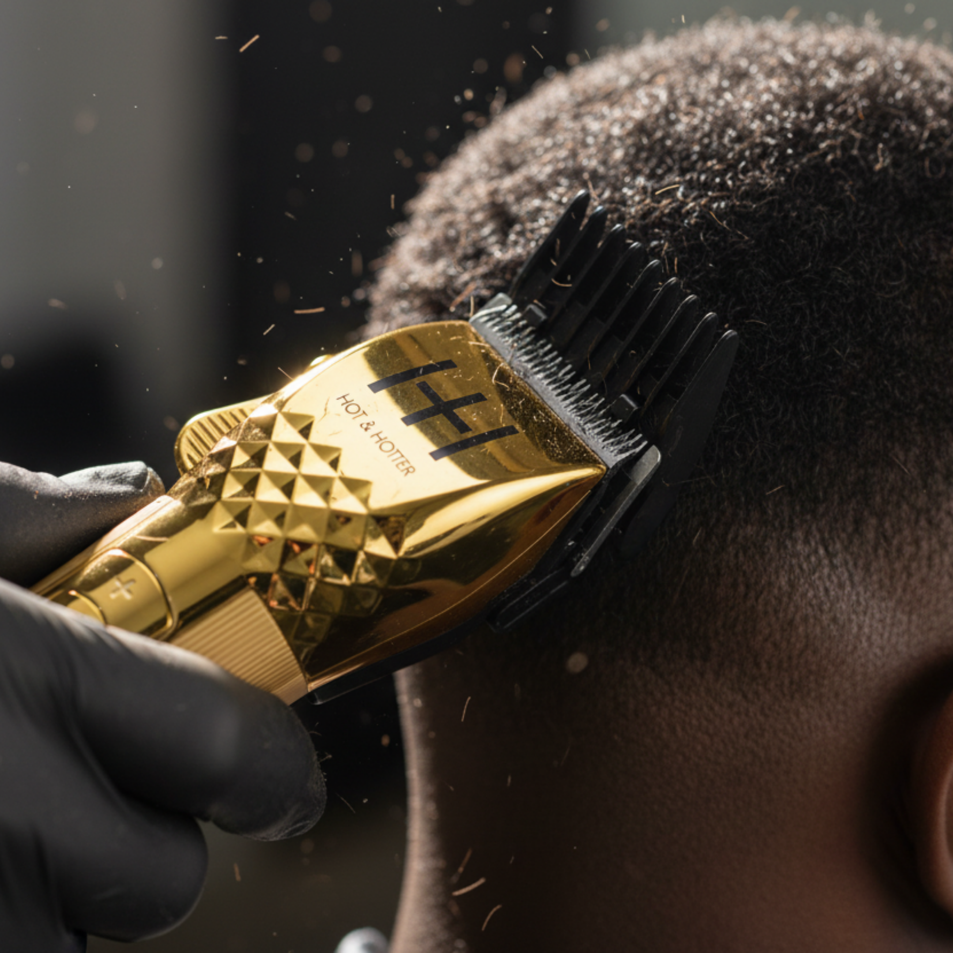 Gold-plated Hot & Hotter cordless clipper trimming curly hair with black guide comb and gloved hand visible