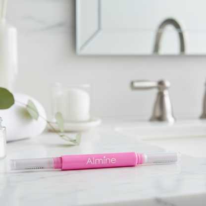 Pink dual-ended Almine precision eyebrow shaper with protective caps resting on white marble bathroom countertop