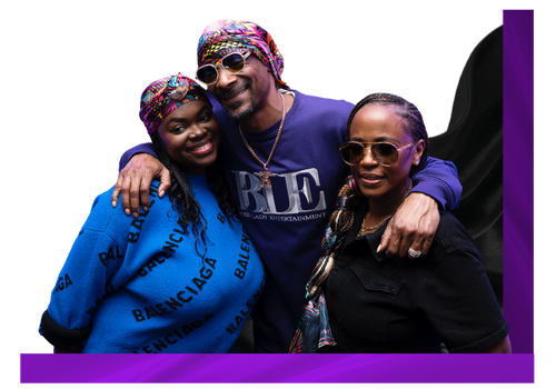 Three smiling adults wearing sunglasses and colorful headscarves posing closely with arms around each other against black background