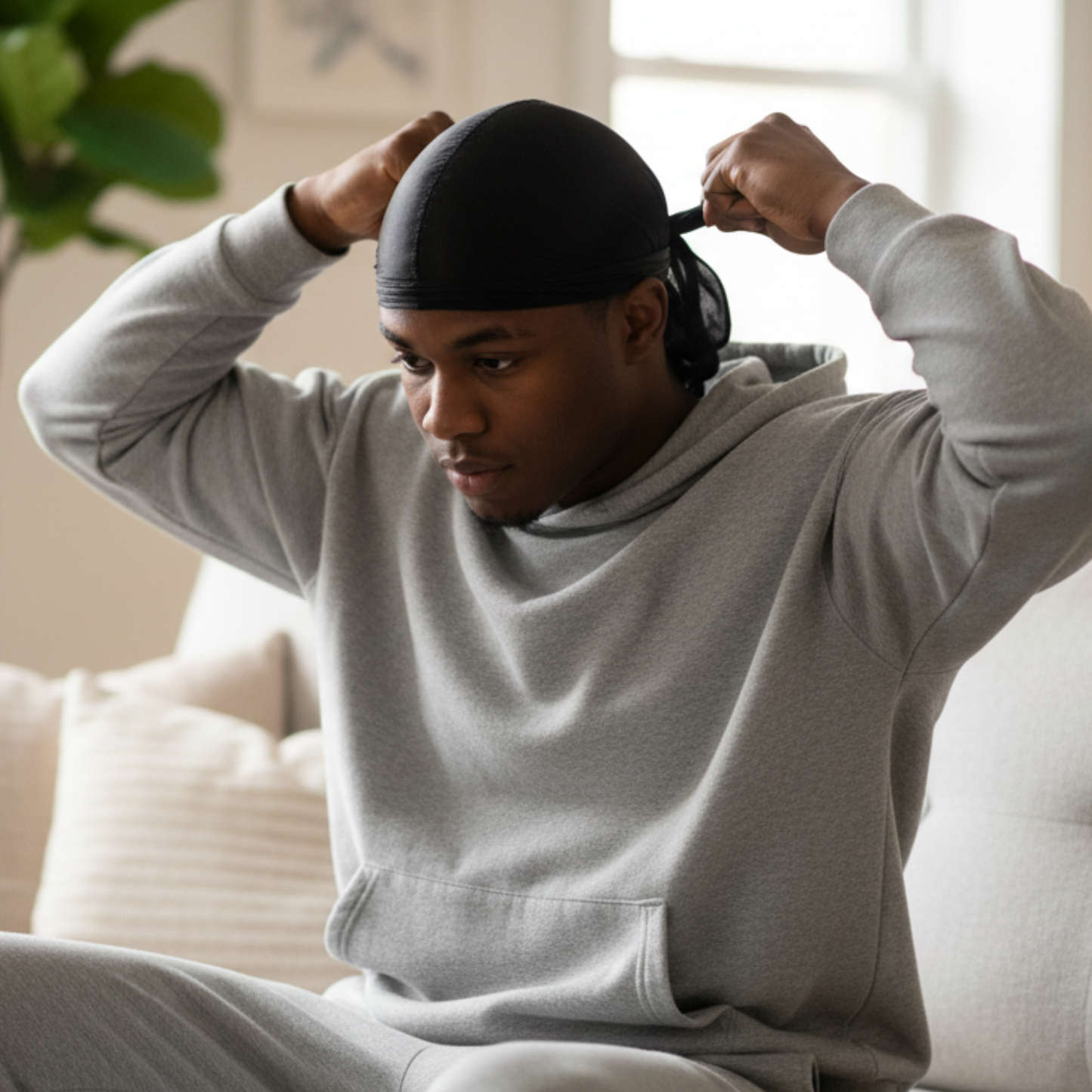 A focused man indoors adjusting Mr. Durag Silky Deluxe Durag, 1 Count, Black, featuring smooth, silky fabric designed for secure fit and durable 360-wave training comfort.