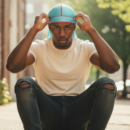 A man sitting outdoors wearing Mr. Durag Silky Deluxe Durag Remix, 1 Count, Assorted Colors in light blue with red trim, designed for 360 wave training and stylish hair protection.