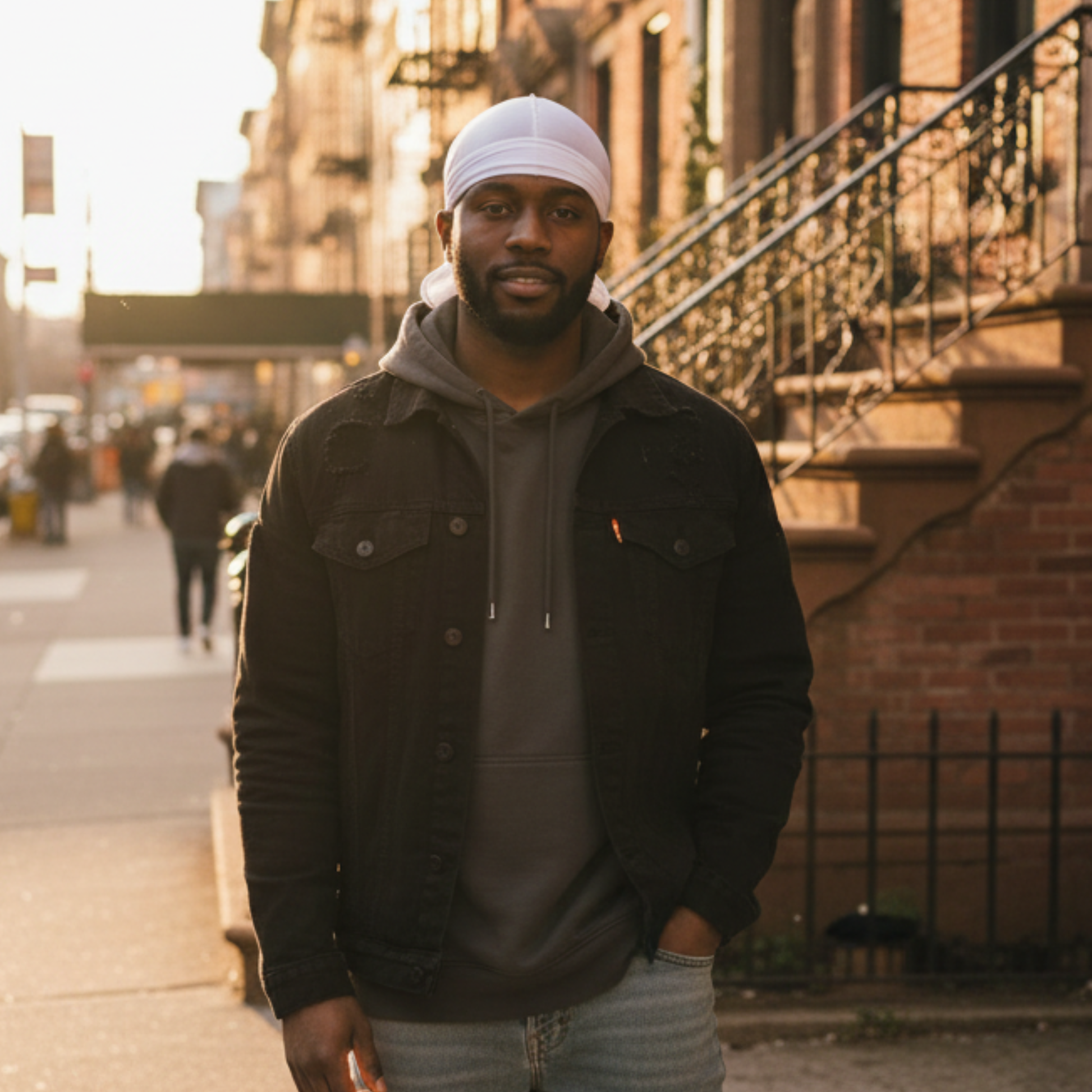A man standing outdoors in soft evening light wearing a Mr. Durag Solid Durag, 1 Count, White styled under a dark jacket and hoodie, demonstrating a sleek look for 360 waves.