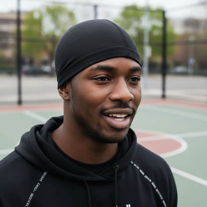 A man outdoors on a basketball court wearing Mr. Durag Spandex Dome Cap, 1 Count, Black, featuring a smooth, breathable fit designed for wave training and active wear comfort.