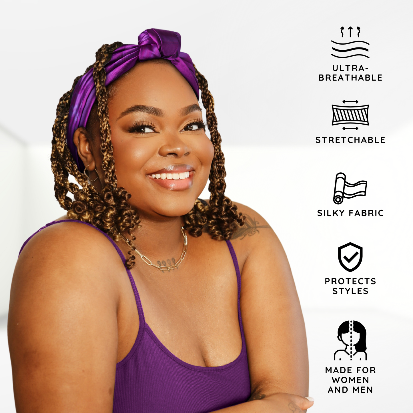 A smiling woman with curly hair wearing a vibrant purple Broadus Collection Headwrap Scarf by Shante & Snoop Dogg, Purple Butterfly, showcasing a silky, stretchable, ultra-breathable fabric designed to protect styles for both women and men.