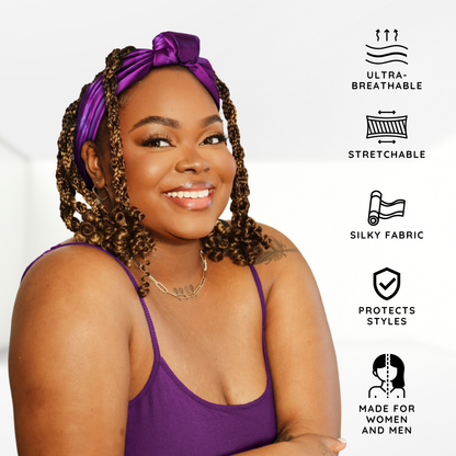 A smiling woman with curly hair wearing a vibrant purple Broadus Collection Headwrap Scarf by Shante & Snoop Dogg, Purple Butterfly, showcasing a silky, stretchable, ultra-breathable fabric designed to protect styles for both women and men.