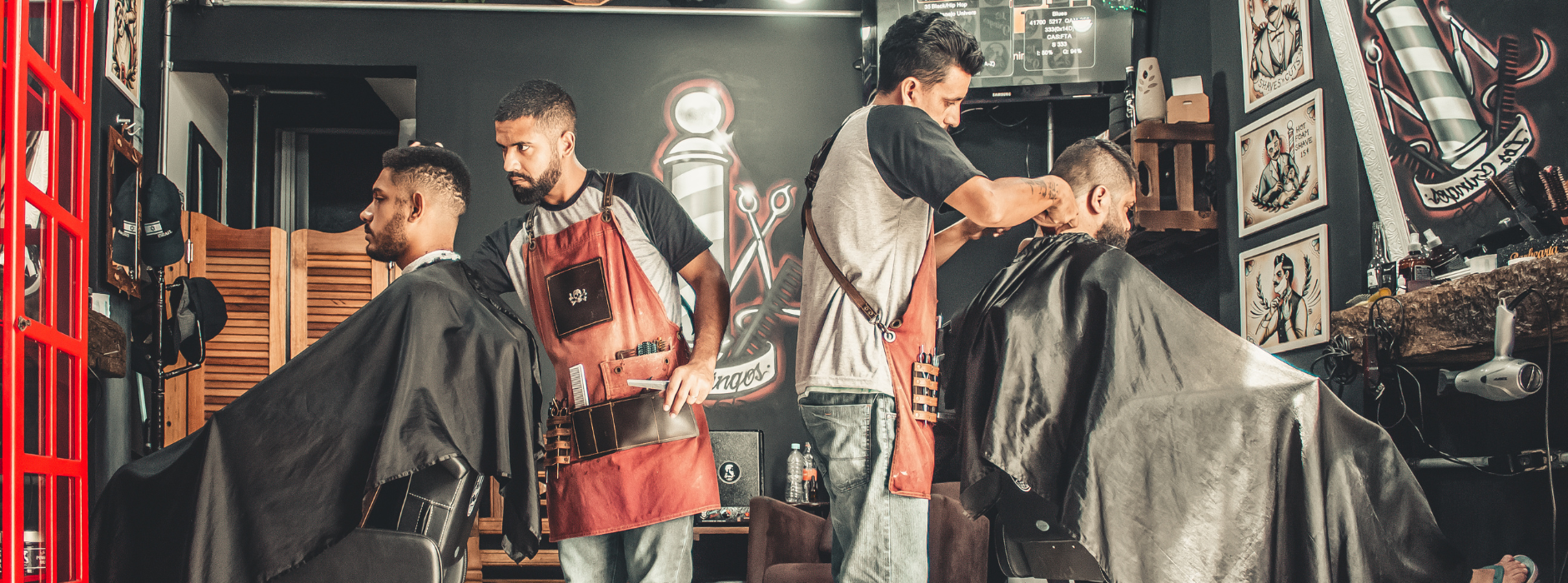 Two barbers cutting hair of male clients inside a modern barbershop with vintage barber tools and dark walls background