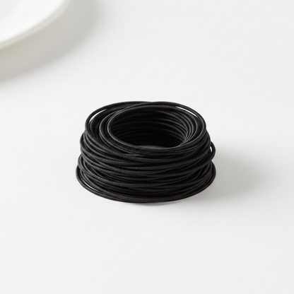 A neat pile of black Annie Tangle Free Ponytailers Thin 3 1/2 Inch, 50 Count, Black arranged on a white surface, designed for secure, snag-free ponytail styling.