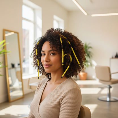 Woman with natural curly hair styled using long yellow flexible hair rollers designed for gentle, snag-free setting on textured and natural hair, in a bright salon setting.